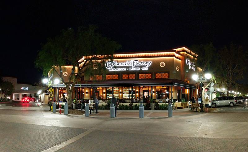 Panoramic night view of a Cheesecake Factory restaurant with its lit sign and patio